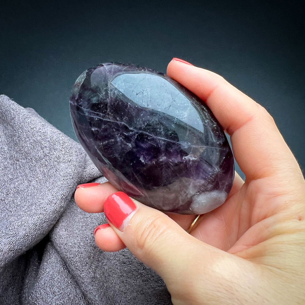 Fluorit Handschmeichler in tiefem Violett mit natürlichen Einschlüssen, glatte polierte Oberfläche, ideal als beruhigender Energiegeber für Meditation und Dekoration.