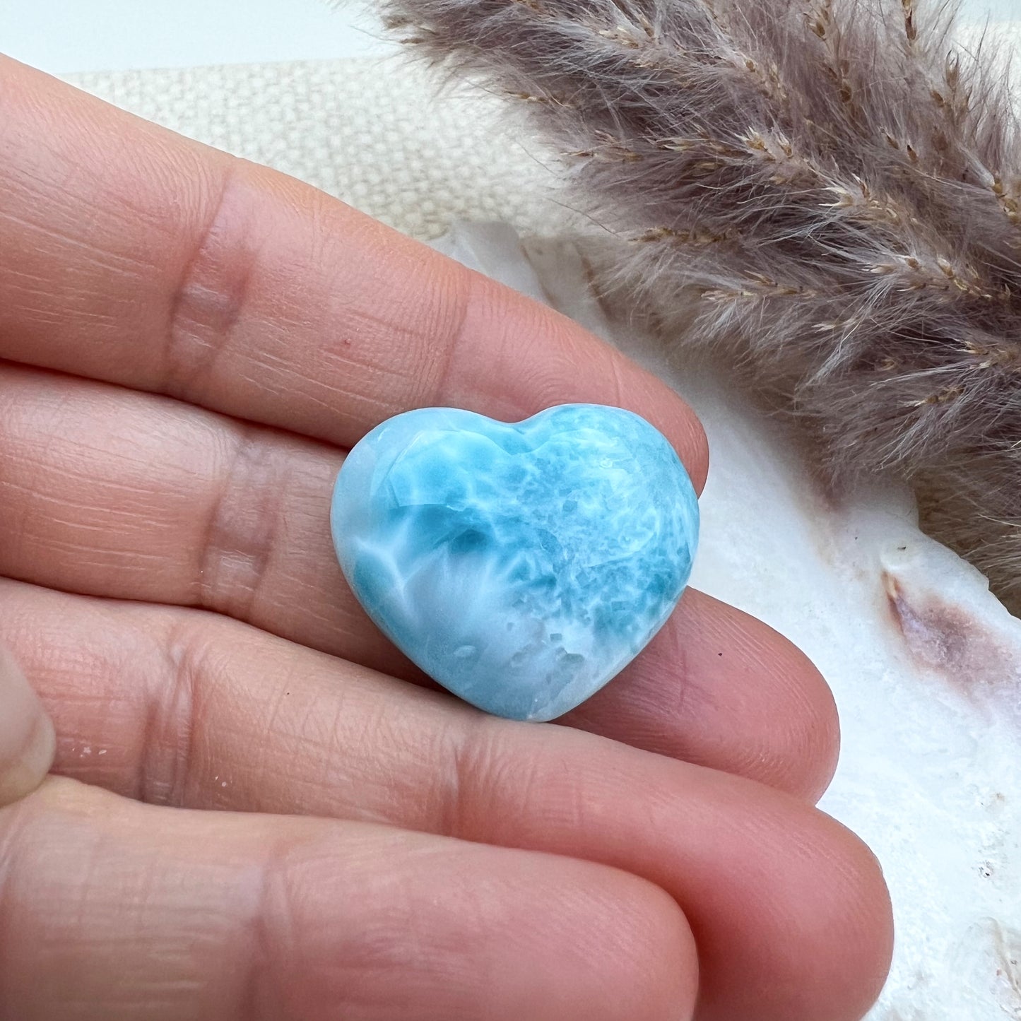 
                  
                    Kleines Larimar Herz in meeresblau mit weißen Akzenten, gehalten in der Hand, zeigt die glatte Oberfläche und einzigartige Maserung des Edelsteins.
                  
                