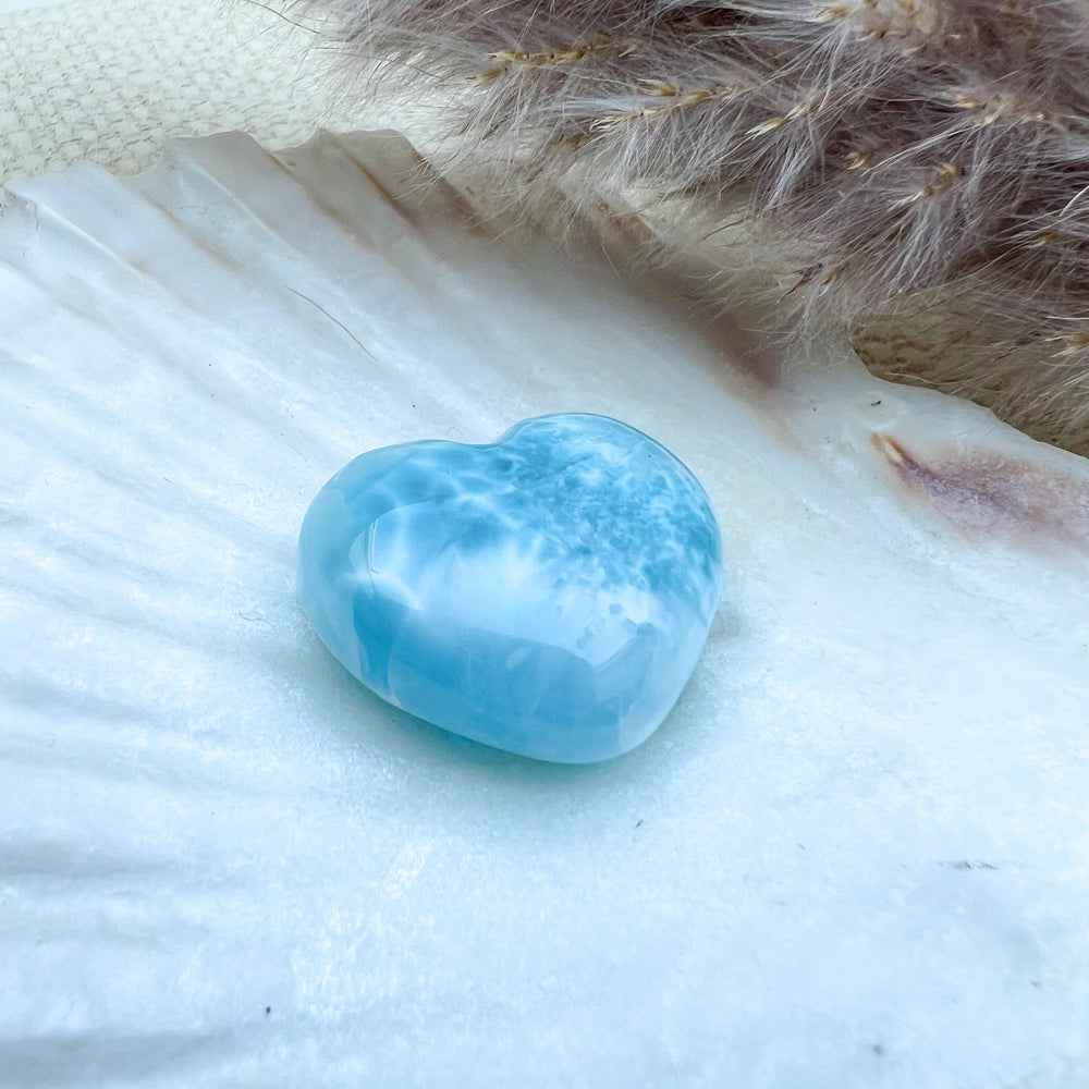 Handgearbeitetes Larimar Herz in meeresblau mit weißen Akzenten, präsentiert auf einer Muschelschale – einzigartiger Edelstein aus der Dominikanischen Republik.