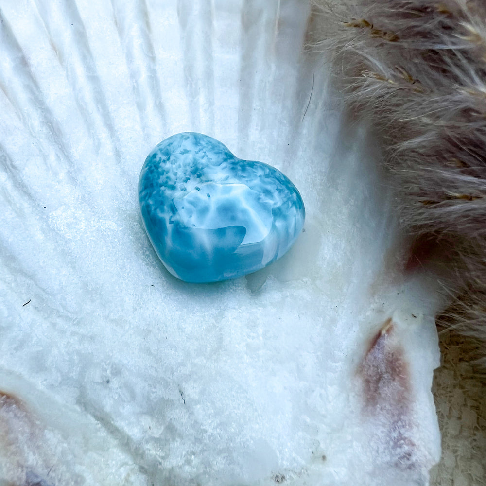 Handgearbeitetes Larimar Herz in meeresblau mit weißen Akzenten, präsentiert auf einer Muschelschale – einzigartiger Edelstein aus der Dominikanischen Republik.