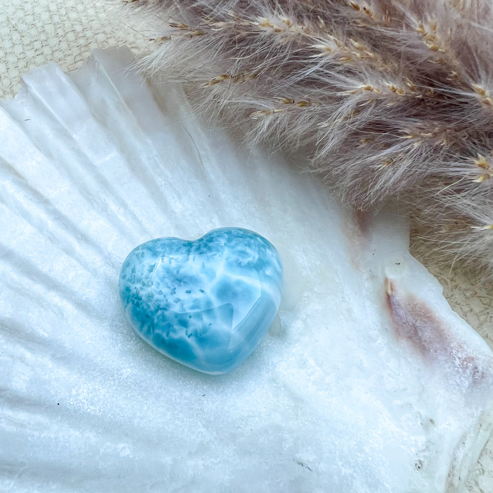 Handgearbeitetes Larimar Herz in meeresblau mit weißen Akzenten, präsentiert auf einer Muschelschale – einzigartiger Edelstein aus der Dominikanischen Republik.