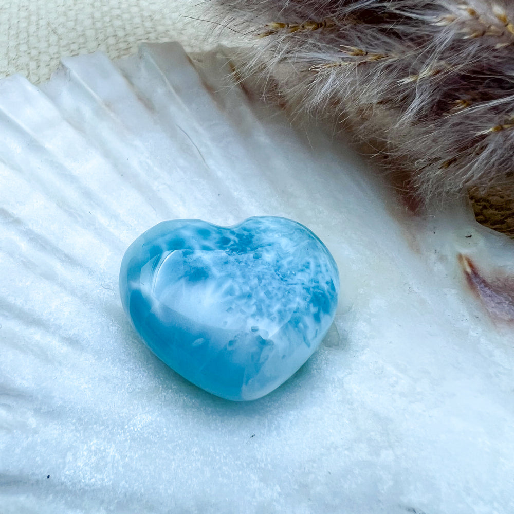 Handgearbeitetes Larimar Herz in meeresblau mit weißen Akzenten, präsentiert auf einer Muschelschale – einzigartiger Edelstein aus der Dominikanischen Republik.