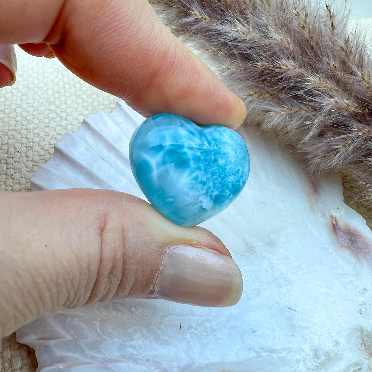 Kleines Larimar Herz in meeresblau mit weißen Akzenten, gehalten in der Hand, zeigt die glatte Oberfläche und einzigartige Maserung des Edelsteins.