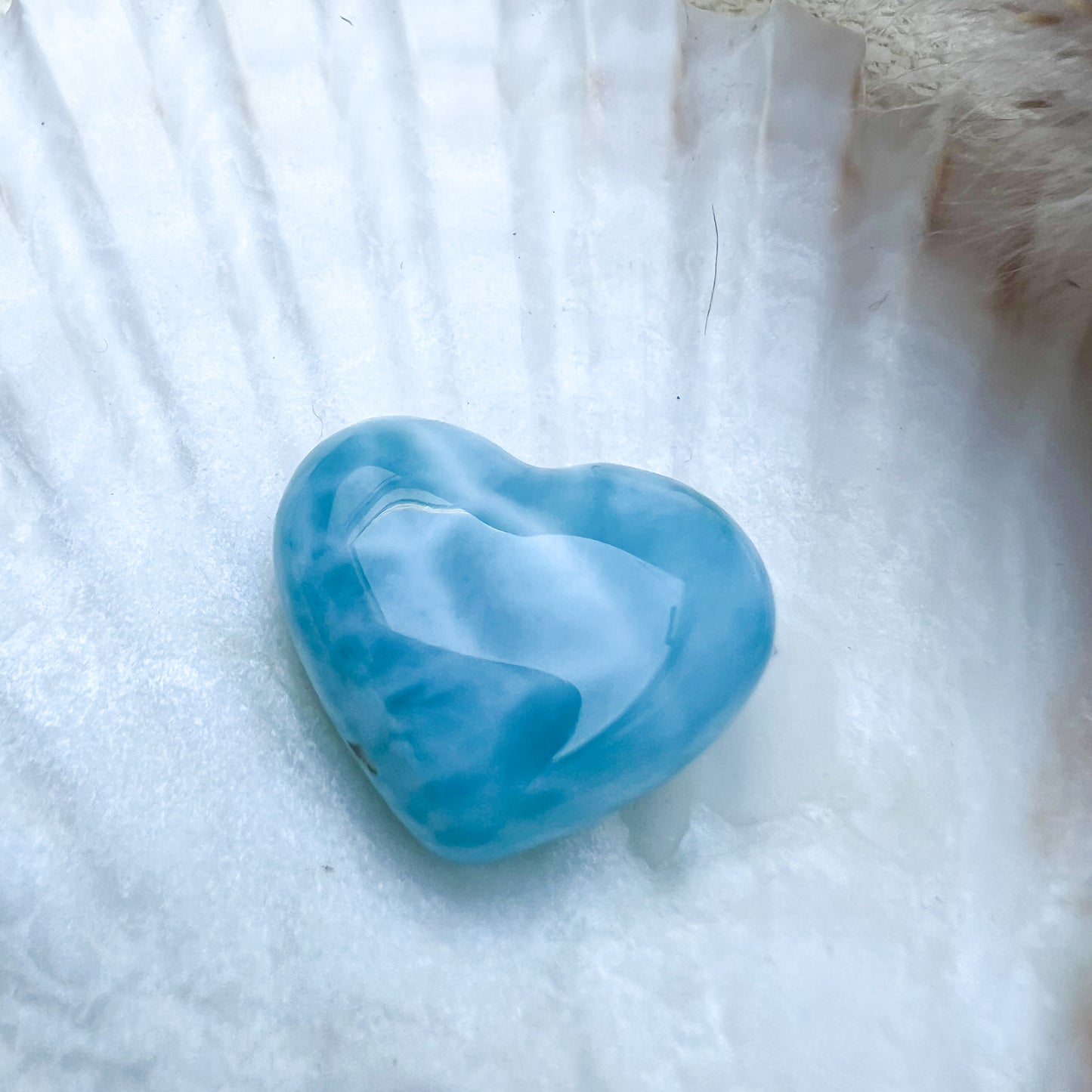 Handgearbeitetes Larimar Herz in meeresblau mit weißen Akzenten, präsentiert auf einer Muschelschale – einzigartiger Edelstein aus der Dominikanischen Republik.