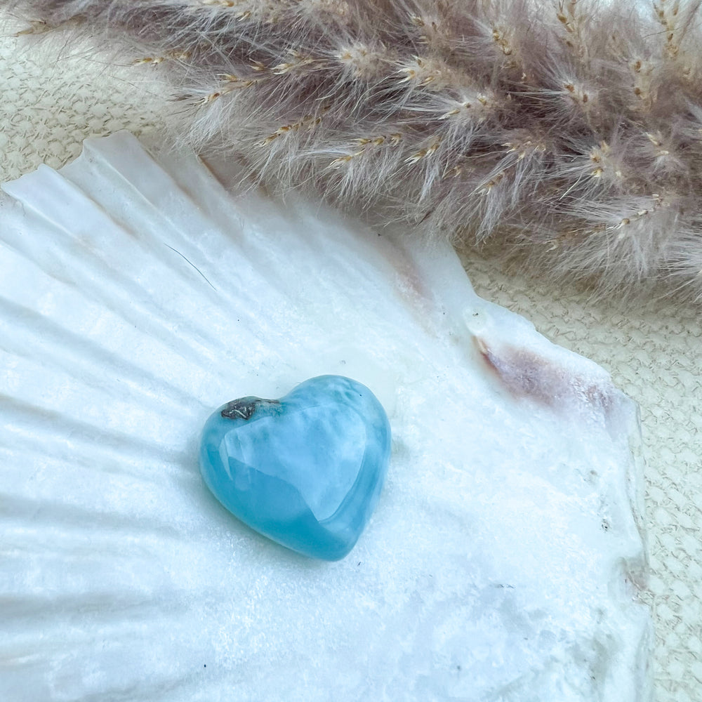 Handgearbeitetes Larimar Herz in meeresblau mit weißen Akzenten, präsentiert auf einer Muschelschale – einzigartiger Edelstein aus der Dominikanischen Republik.