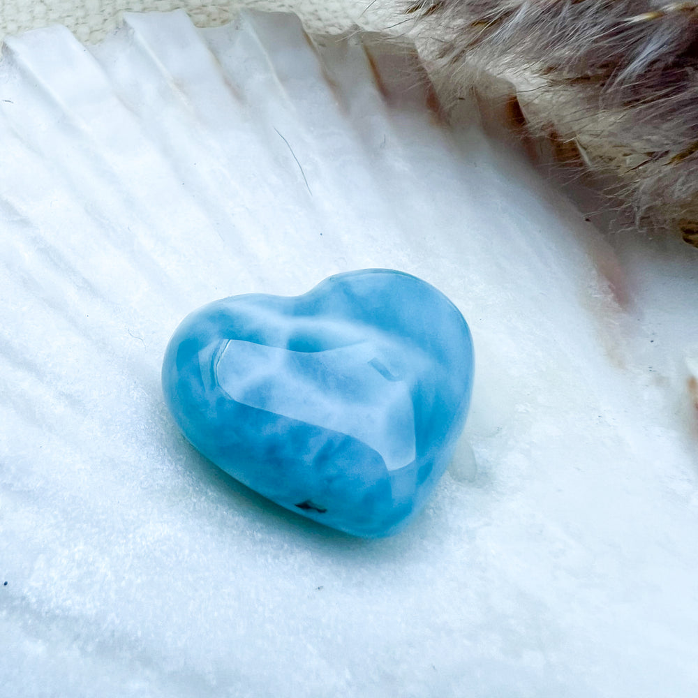 Handgearbeitetes Larimar Herz in meeresblau mit weißen Akzenten, präsentiert auf einer Muschelschale – einzigartiger Edelstein aus der Dominikanischen Republik.