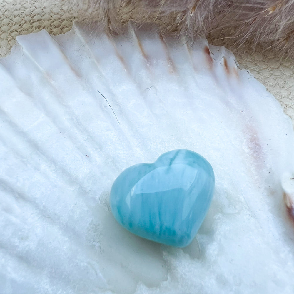 Handgearbeitetes Larimar Herz in meeresblau mit weißen Akzenten, präsentiert auf einer Muschelschale – einzigartiger Edelstein aus der Dominikanischen Republik