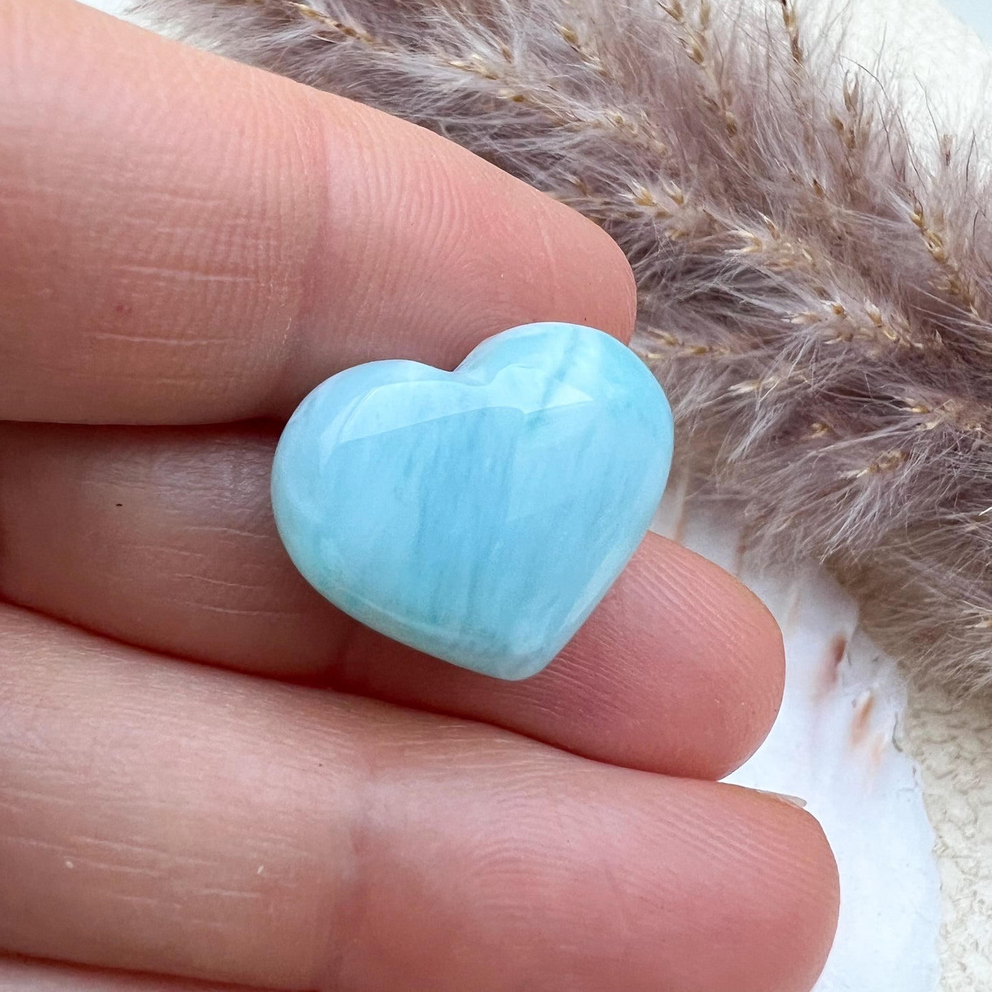 Kleines Larimar Herz in meeresblau mit weißen Akzenten, gehalten in der Hand, zeigt die glatte Oberfläche und einzigartige Maserung des Edelsteins.