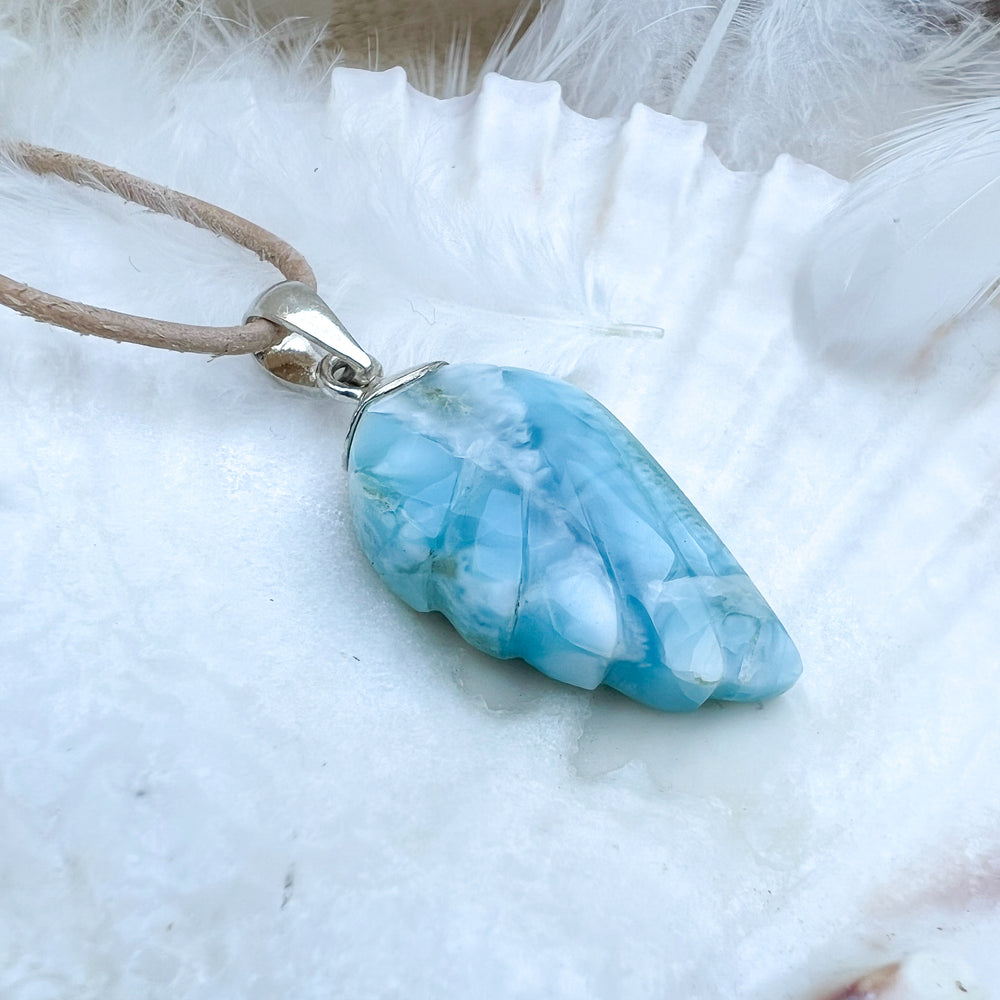 
                  
                    Larimar Engelsflügel-Anhänger aus 925er Sterlingsilber, präsentiert auf einer weißen Muschelschale, umgeben von Federn, mit natürlichem Lederband – ein himmlisches Schmuckstück.
                  
                