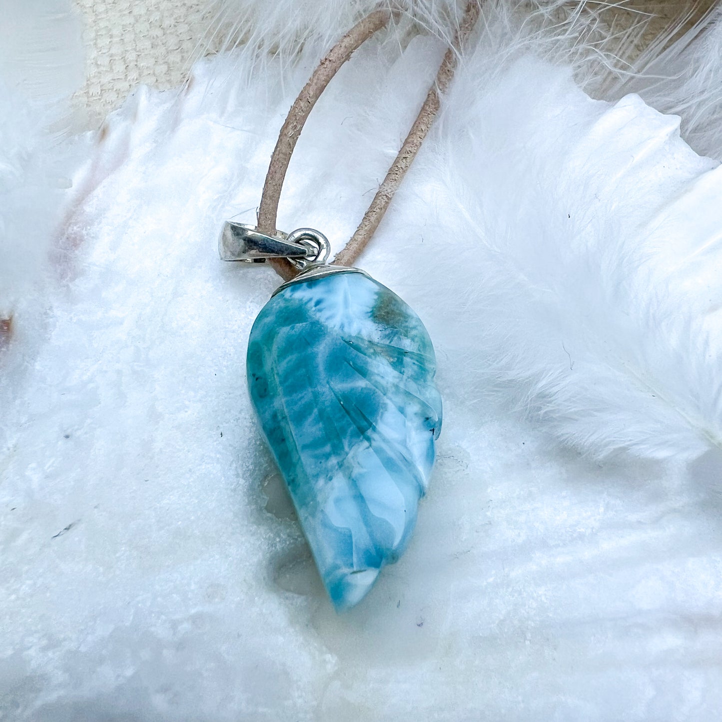 
                  
                    Larimar Engelsflügel-Anhänger aus 925er Sterlingsilber, präsentiert auf einer weißen Muschelschale, umgeben von Federn, mit natürlichem Lederband – ein himmlisches Schmuckstück.
                  
                