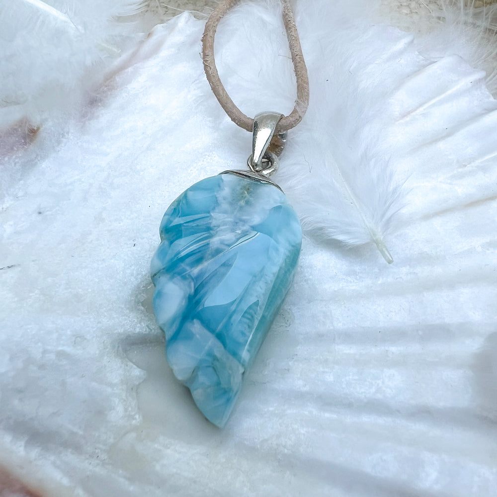 
                  
                    Larimar Engelsflügel-Anhänger aus 925er Sterlingsilber, präsentiert auf einer weißen Muschelschale, umgeben von Federn, mit natürlichem Lederband – ein himmlisches Schmuckstück.
                  
                