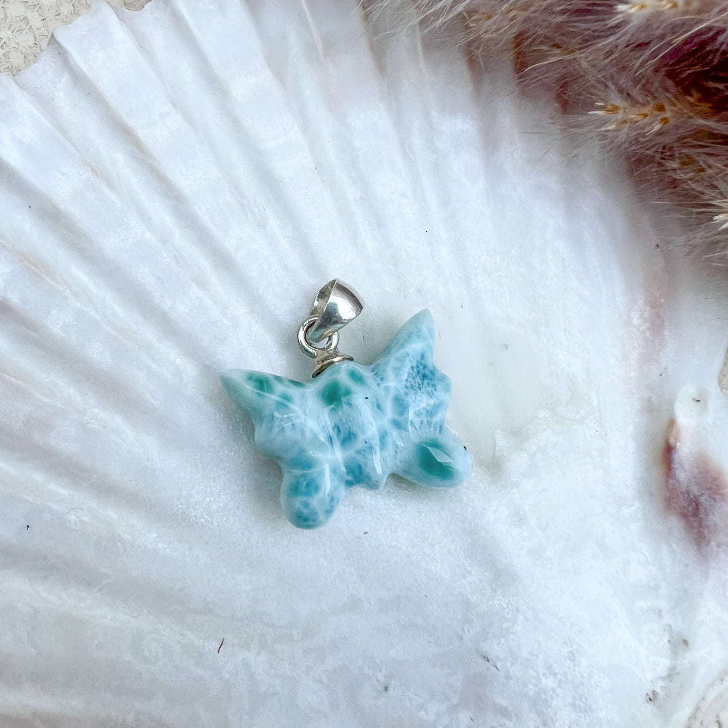 Larimar Schmetterlings-Anhänger aus 925er Sterlingsilber, handgefertigt, in meeresblau mit weißen Akzenten, präsentiert auf einer weißen Muschelschale – ein Unikat mit einzigartigen Farbverläufen.