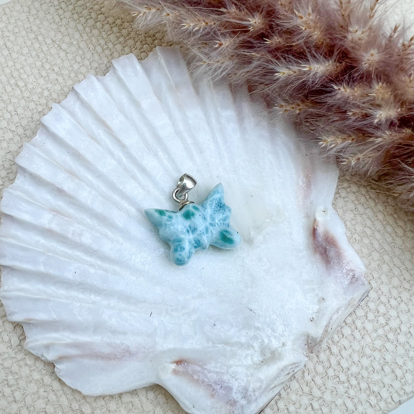 
                  
                    Larimar Schmetterlings-Anhänger aus 925er Sterlingsilber, handgefertigt, in meeresblau mit weißen Akzenten, präsentiert auf einer weißen Muschelschale – ein Unikat mit einzigartigen Farbverläufen.
                  
                