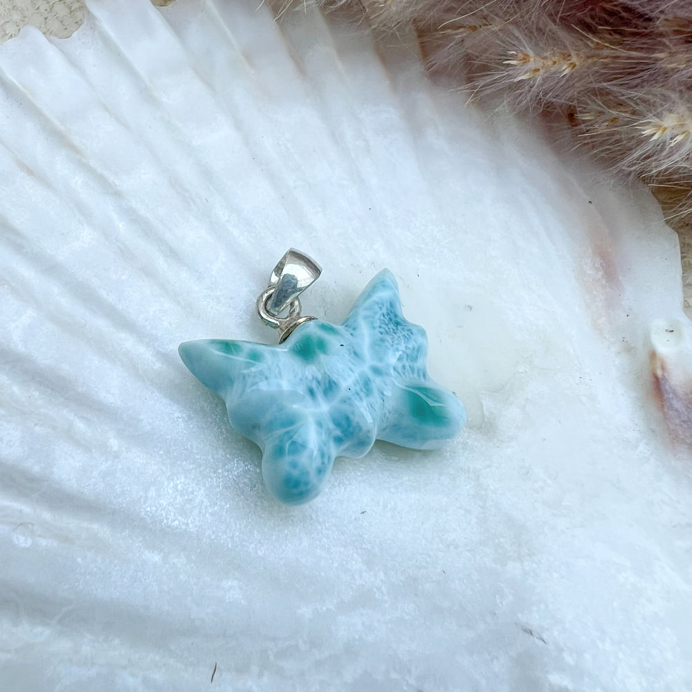 Larimar Schmetterlings-Anhänger aus 925er Sterlingsilber, handgefertigt, in meeresblau mit weißen Akzenten, präsentiert auf einer weißen Muschelschale – ein Unikat mit einzigartigen Farbverläufen.