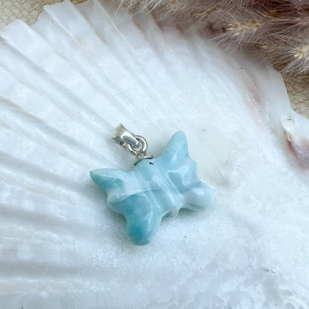 
                  
                    Larimar Schmetterlings-Anhänger aus 925er Sterlingsilber, handgefertigt, in meeresblau mit weißen Akzenten, präsentiert auf einer weißen Muschelschale – ein Unikat mit einzigartigen Farbverläufen.
                  
                