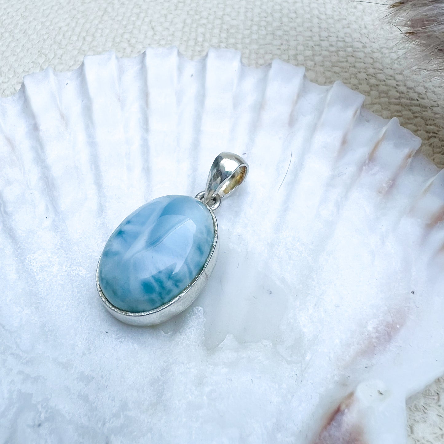 Ovaler Larimar-Anhänger aus 925er Sterlingsilber, Vorderseite des Steins in hellblauer Farbe mit zarten weißen Schattierungen, präsentiert auf einer Muschelschale.