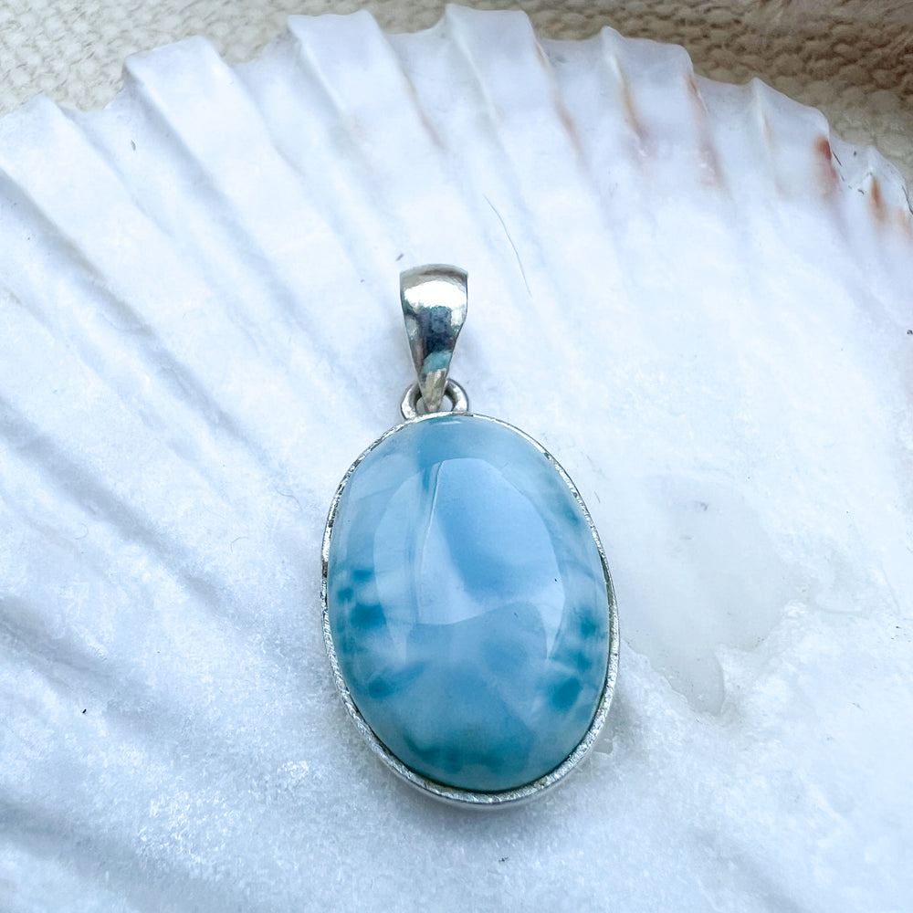 Ovaler Larimar-Anhänger aus 925er Sterlingsilber, Vorderseite des Steins in hellblauer Farbe mit zarten weißen Schattierungen, präsentiert auf einer Muschelschale.