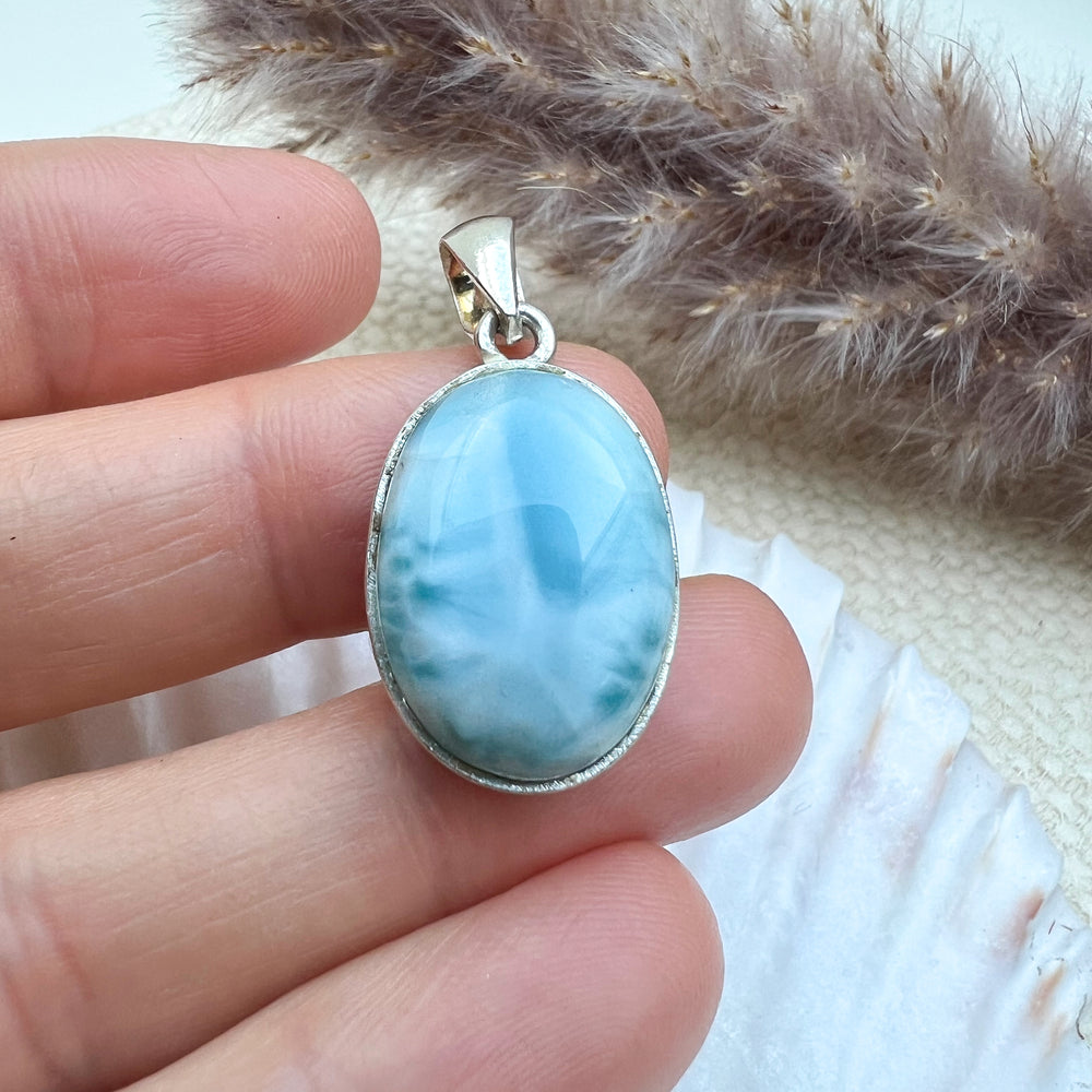 Ovaler Larimar-Anhänger aus 925er Sterlingsilber, gehalten in der Hand, um die Details und Größe des Edelsteins zu zeigen, mit natürlicher Maserung und polierter Oberfläche.