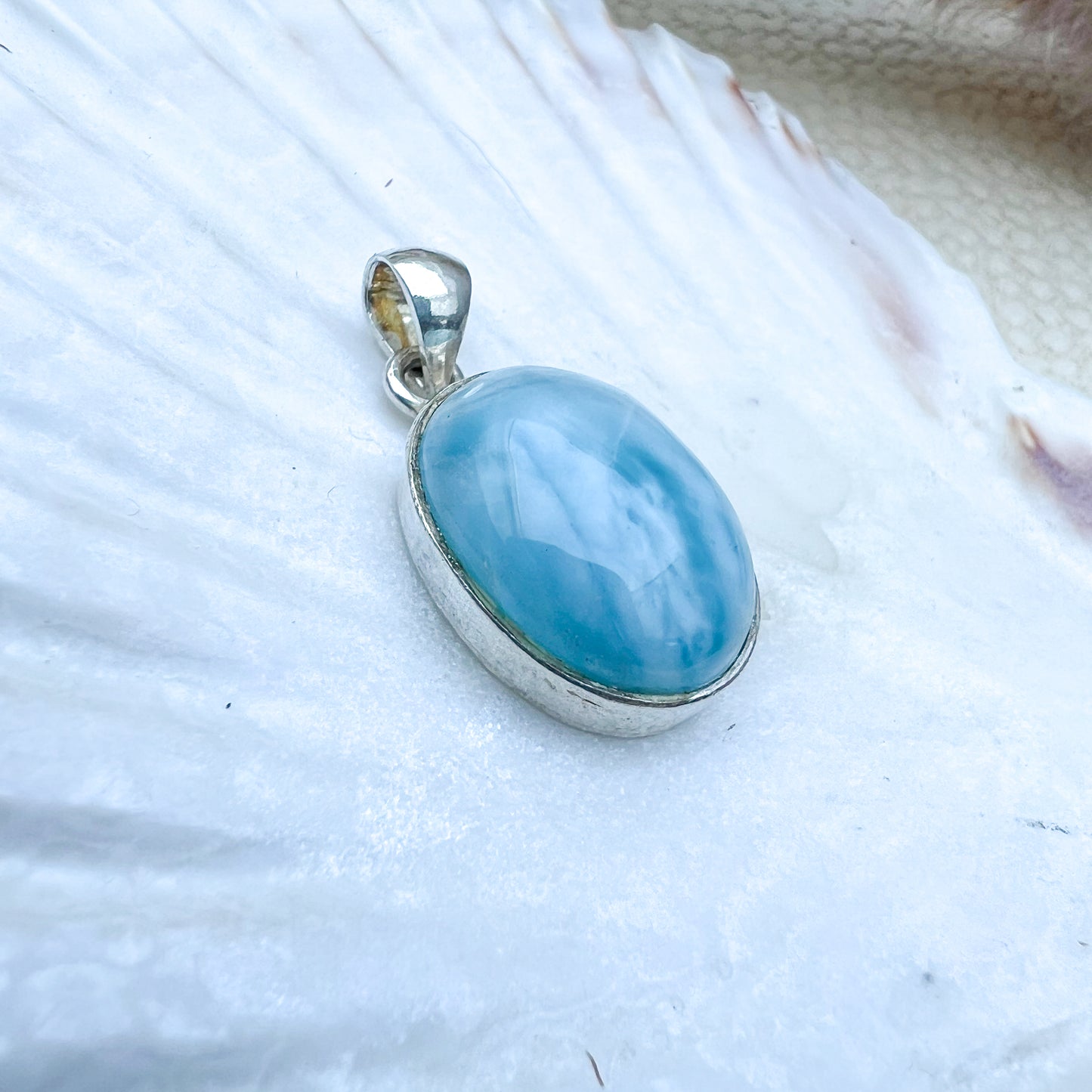 Ovaler Larimar-Anhänger aus 925er Sterlingsilber, Vorderseite des Steins in hellblauer Farbe mit zarten weißen Schattierungen, präsentiert auf einer Muschelschale.