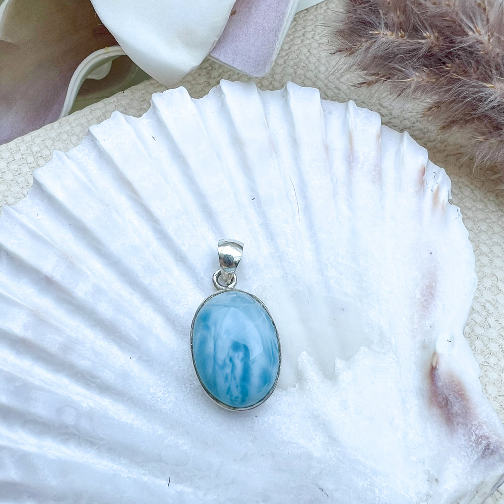 Ovaler Larimar-Anhänger aus 925er Sterlingsilber, Vorderseite des Steins in hellblauer Farbe mit zarten weißen Schattierungen, präsentiert auf einer Muschelschale.