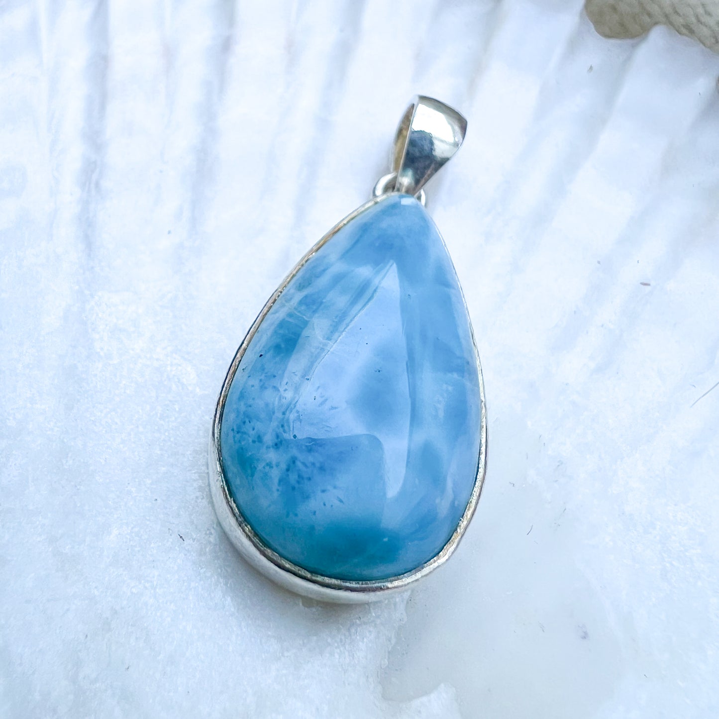 
                  
                    Larimar Tropfen-Anhänger aus 925er Sterlingsilber, präsentiert auf einer weißen Muschelschale, mit einer glatten, glänzenden Oberfläche und lebhaften Blau-Tönen.
                  
                