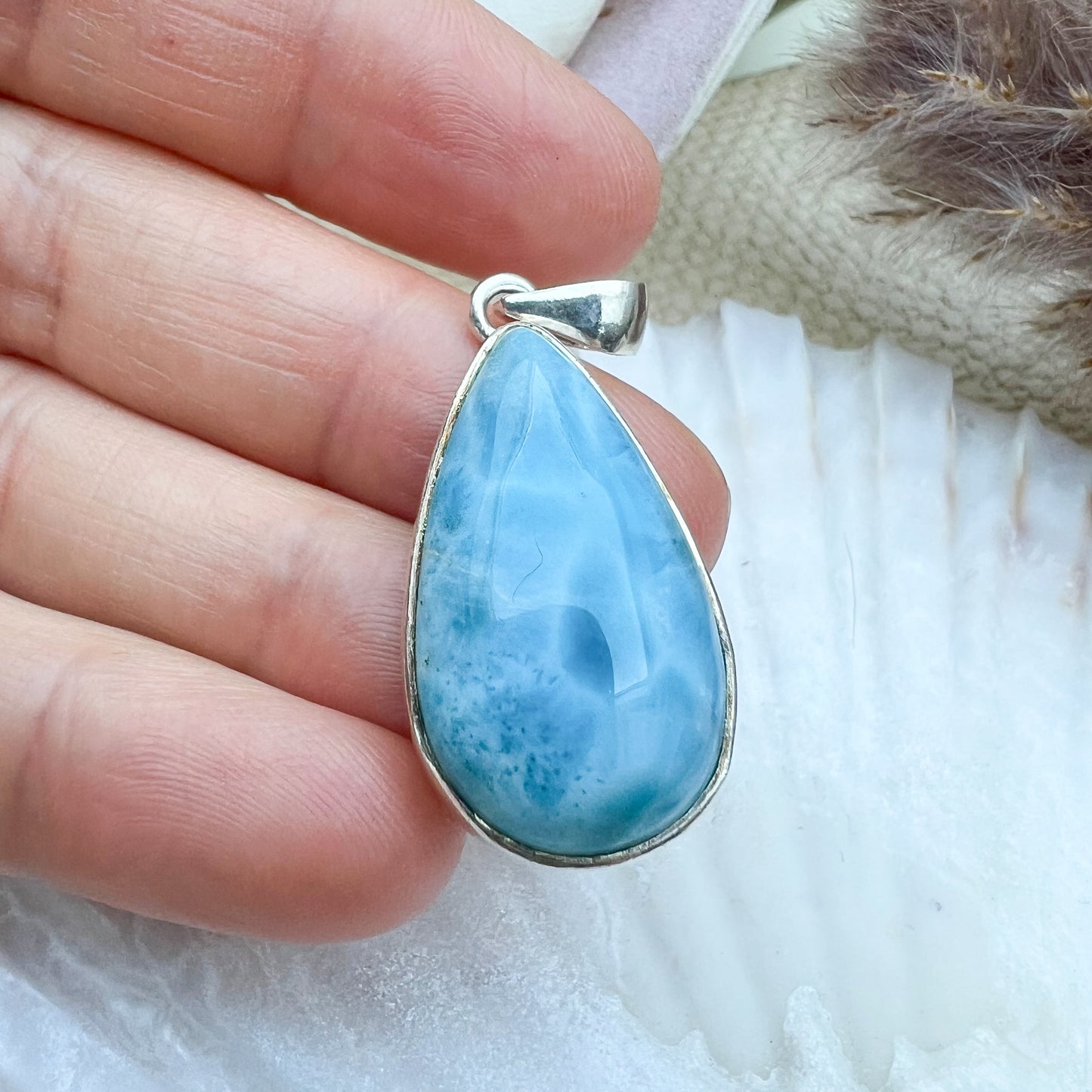 
                  
                    Larimar Tropfen-Anhänger aus 925er Sterlingsilber, gehalten in der Hand, zeigt die polierte Oberfläche und die einzigartigen blauen Musterungen des Edelsteins.
                  
                