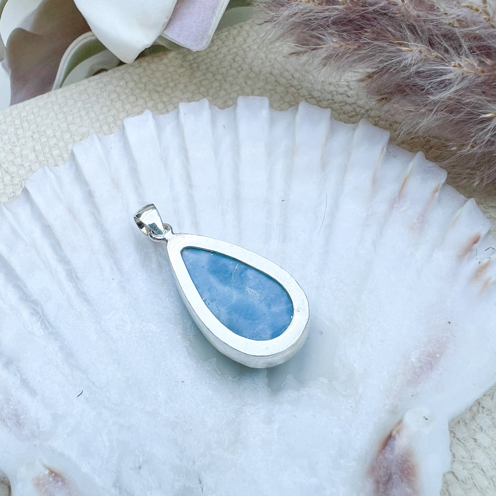 Rückseite des Larimar Tropfen-Anhängers aus 925er Sterlingsilber, präsentiert auf einer Muschelschale, zeigt den eingefassten Edelstein mit schlichter Verarbeitung.