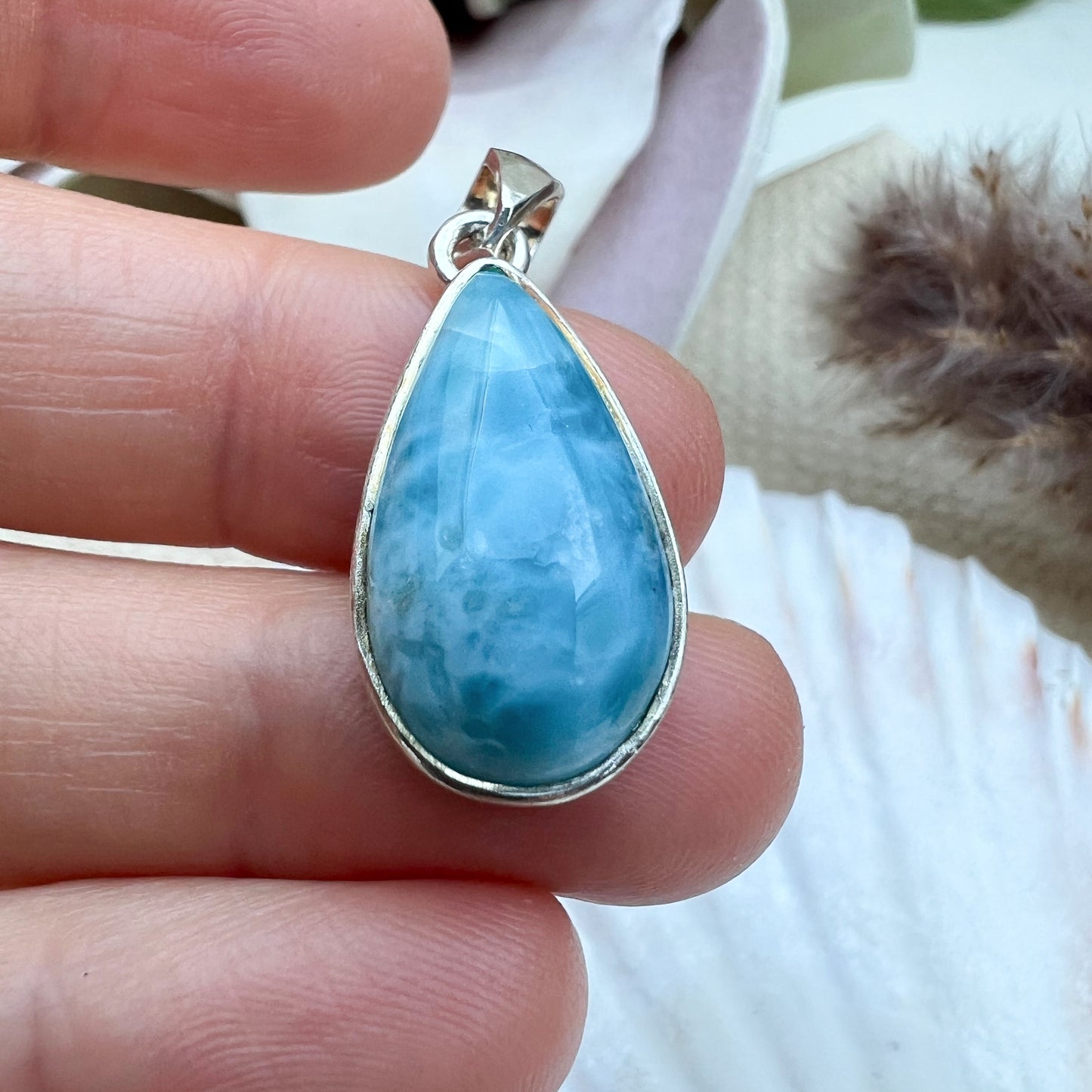 Larimar Tropfen-Anhänger aus 925er Sterlingsilber, gehalten in der Hand, zeigt die polierte Oberfläche und die einzigartigen blauen Musterungen des Edelsteins.