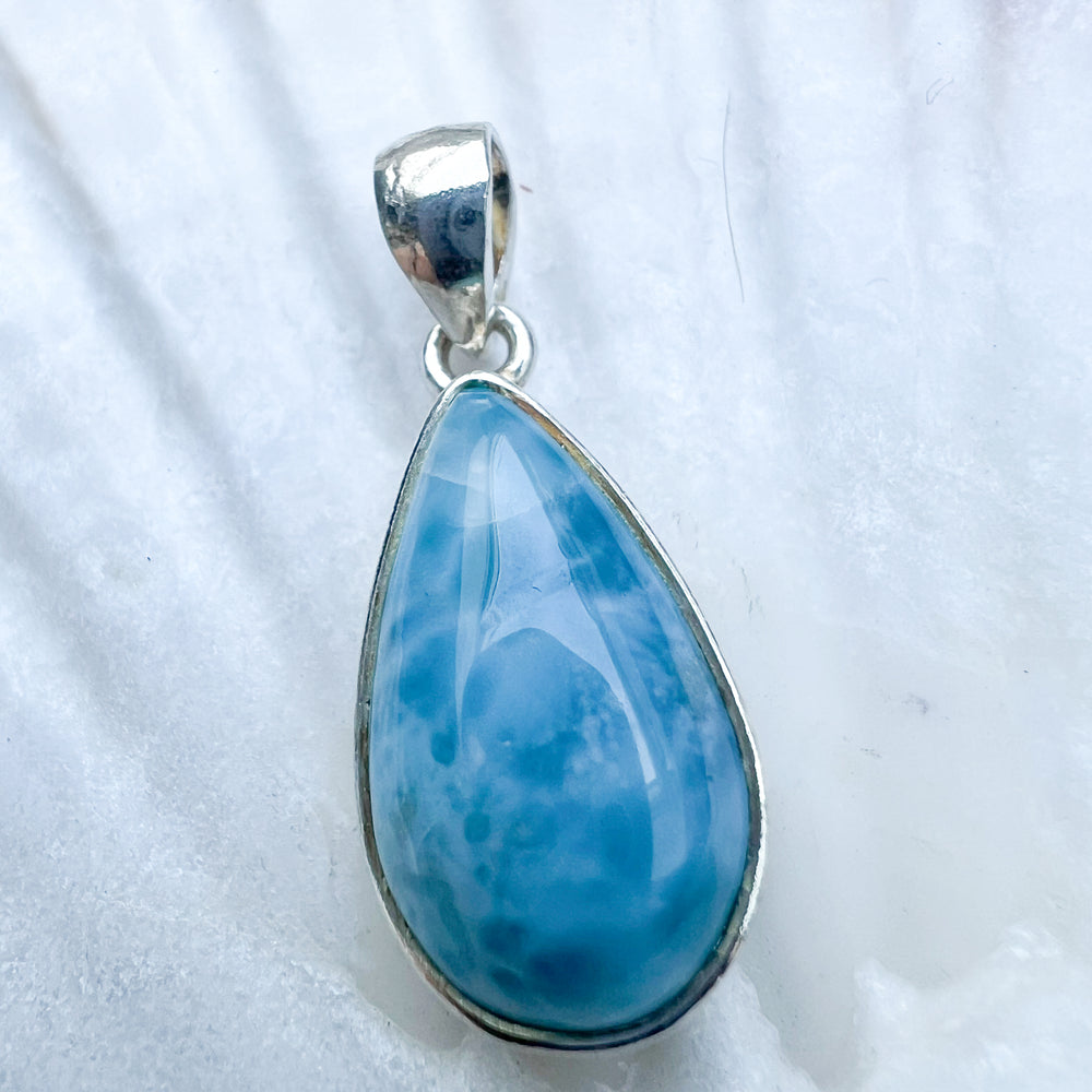 
                  
                    Larimar Tropfen-Anhänger aus 925er Sterlingsilber, präsentiert auf einer weißen Muschelschale, mit einer glatten, glänzenden Oberfläche und lebhaften Blau-Tönen
                  
                