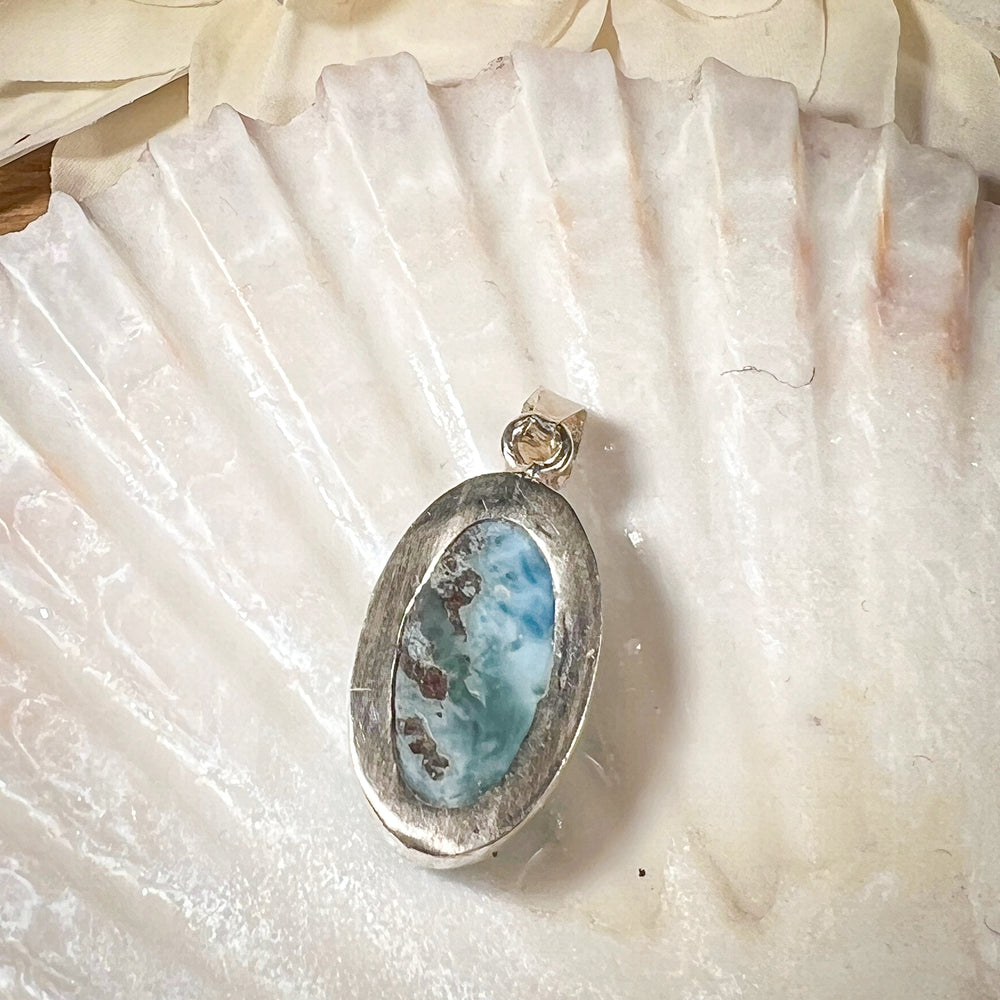 
                  
                    Ovaler Larimar-Kettenanhänger in 925er Sterlingsilber, auf einer Muschelschale präsentiert. Der blau-weiße Edelstein besticht durch natürliche Farbverläufe und erinnert an das karibische Meer. Einzigartiges Schmuckstück für Damen.
                  
                