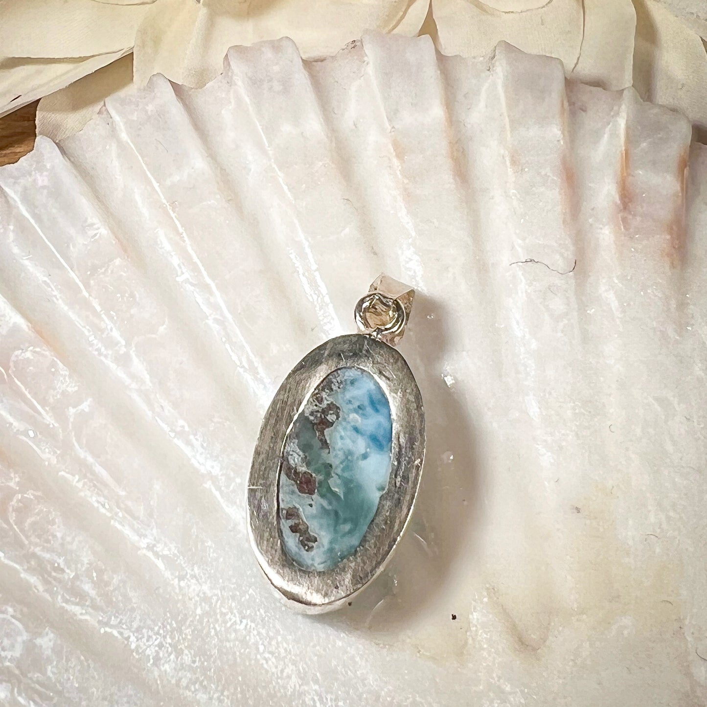 
                  
                    Ovaler Larimar-Kettenanhänger in 925er Sterlingsilber, auf einer Muschelschale präsentiert. Der blau-weiße Edelstein besticht durch natürliche Farbverläufe und erinnert an das karibische Meer. Einzigartiges Schmuckstück für Damen.
                  
                