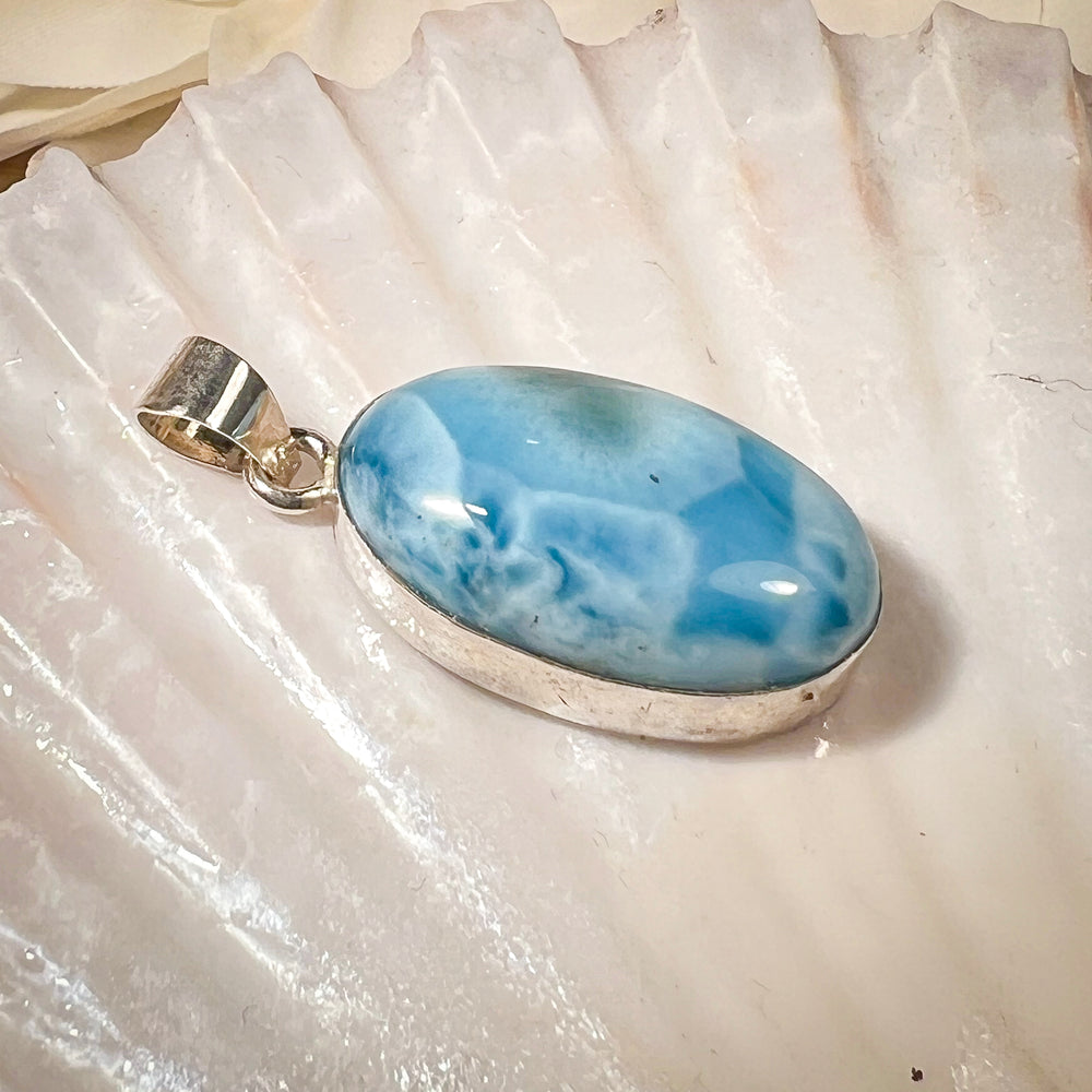 
                  
                    Ovaler Larimar-Kettenanhänger in 925er Sterlingsilber, auf einer Muschelschale präsentiert. Der blau-weiße Edelstein besticht durch natürliche Farbverläufe und erinnert an das karibische Meer. Einzigartiges Schmuckstück für Damen.
                  
                