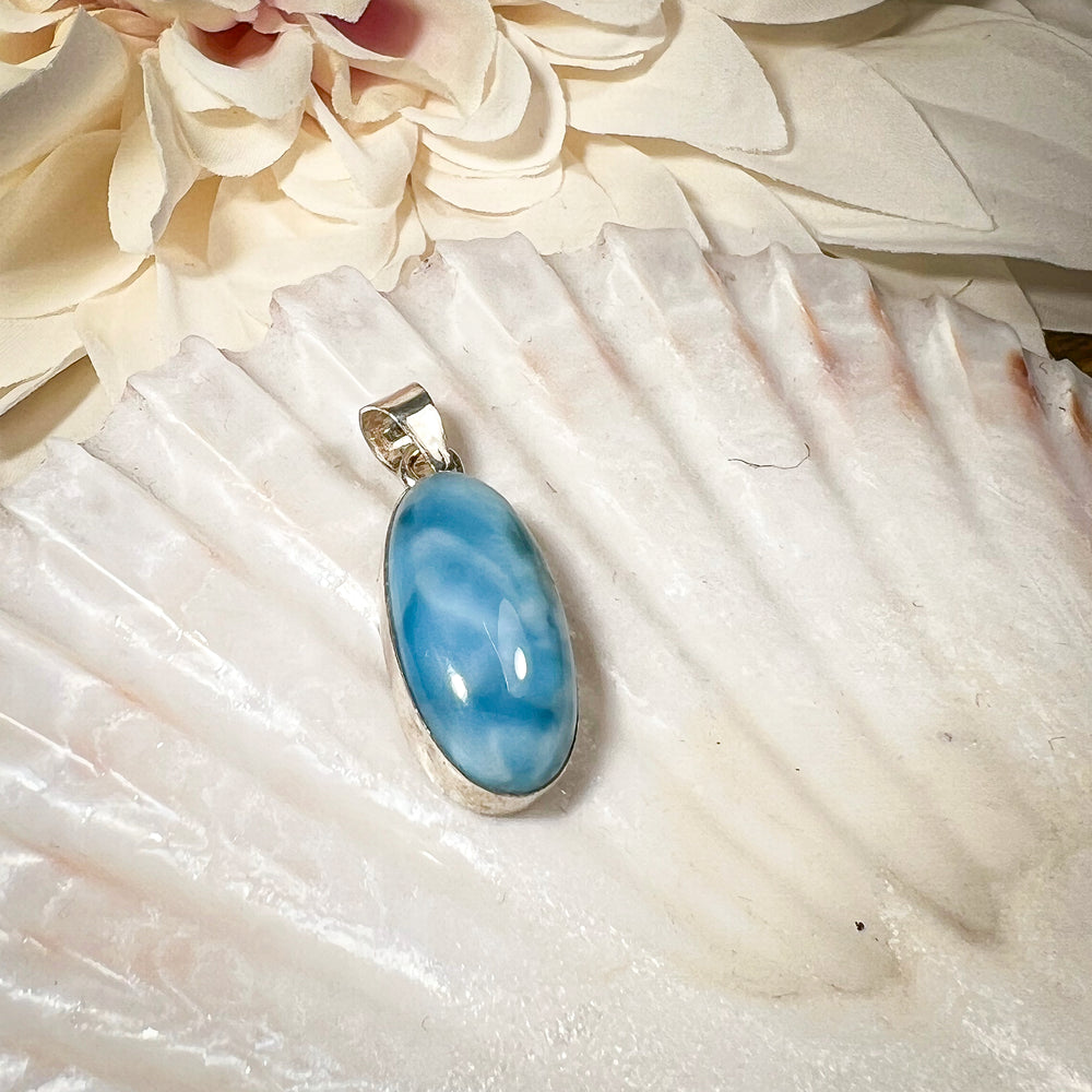 
                  
                    Ovaler Larimar-Kettenanhänger in 925er Sterlingsilber, auf einer Muschelschale präsentiert. Der blau-weiße Edelstein besticht durch natürliche Farbverläufe und erinnert an das karibische Meer. Einzigartiges Schmuckstück für Damen.
                  
                