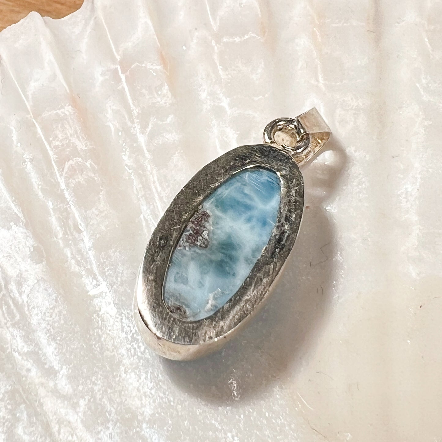 
                  
                    Ovaler Larimar-Kettenanhänger in 925er Sterlingsilber, auf einer Muschelschale präsentiert. Der blau-weiße Edelstein besticht durch natürliche Farbverläufe und erinnert an das karibische Meer. Einzigartiges Schmuckstück für Damen.
                  
                