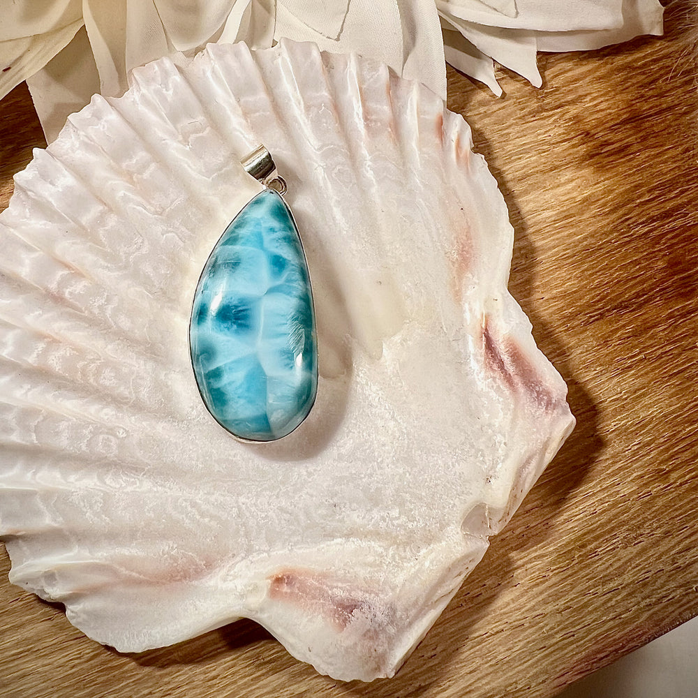 Eleganter Larimar-Anhänger in Tropfenform, gefasst in hochwertigem Silber, präsentiert auf einer Muschelschale. Der hellblaue Edelstein mit natürlicher Maserung wirkt beruhigend und erinnert an die Farben des Meeres. Ideal als einzigartiges Schmuckstück für spirituelle und modebewusste Träger. Hochwertiger Larimar-Anhänger für Damen, perfekt als Geschenk oder für besondere Anlässe.