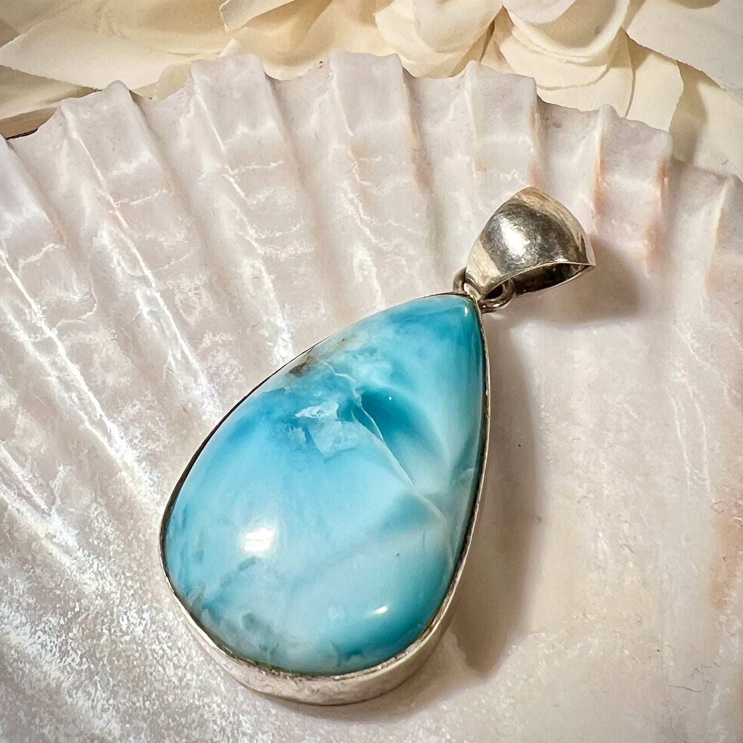 Hochwertiger Larimar-Anhänger in Tropfenform, gefasst in glänzendem Silber, präsentiert auf einer Muschelschale. Der himmelblaue Larimar-Edelstein mit natürlichen Farbverläufen und Maserungen verleiht dem Schmuckstück eine besondere Eleganz. Idealer Edelsteinanhänger für Damen, der maritimes Flair und eine spirituelle Note vereint – perfekt als stilvolles Accessoire oder besonderes Geschenk.