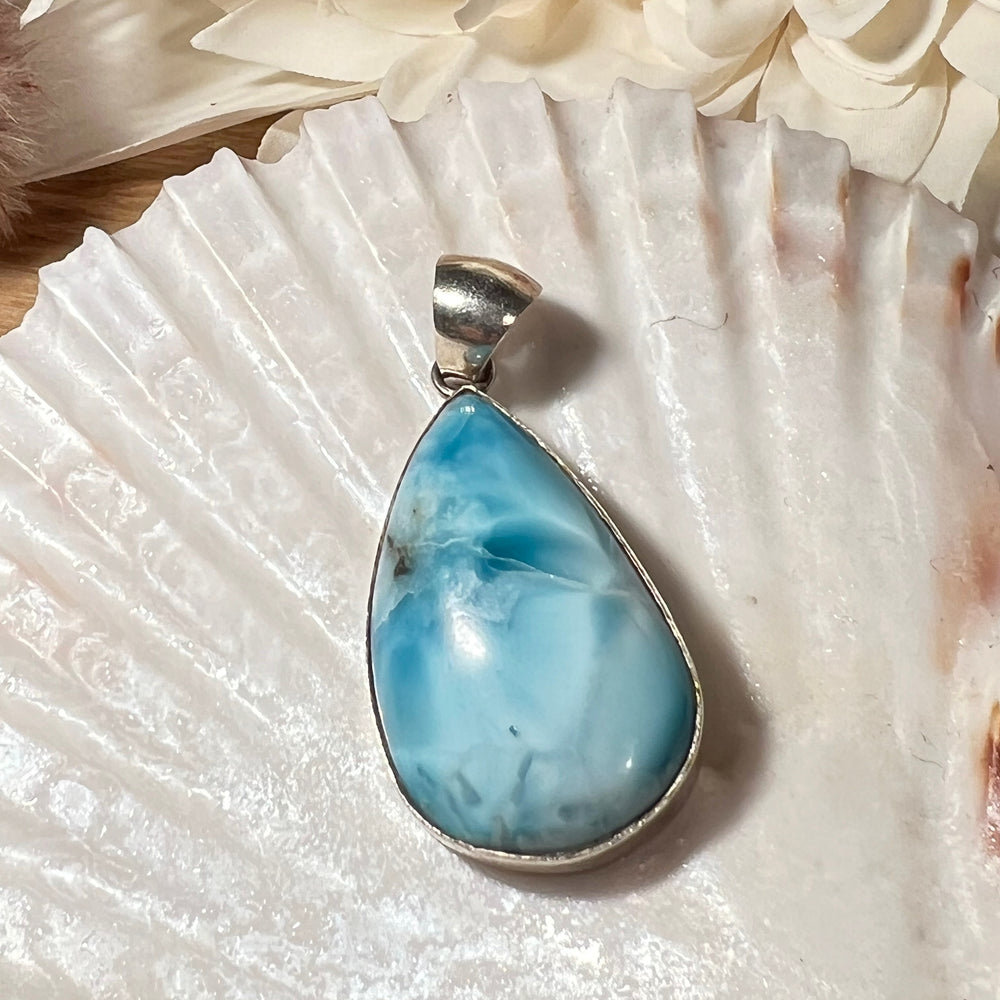 Hochwertiger Larimar-Anhänger in Tropfenform, gefasst in glänzendem Silber, präsentiert auf einer Muschelschale. Der himmelblaue Larimar-Edelstein mit natürlichen Farbverläufen und Maserungen verleiht dem Schmuckstück eine besondere Eleganz. Idealer Edelsteinanhänger für Damen, der maritimes Flair und eine spirituelle Note vereint – perfekt als stilvolles Accessoire oder besonderes Geschenk.