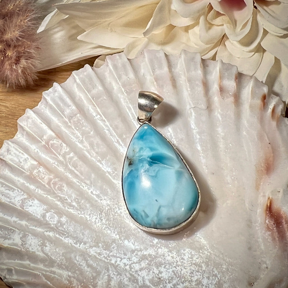 Hochwertiger Larimar-Anhänger in Tropfenform, gefasst in glänzendem Silber, präsentiert auf einer Muschelschale. Der himmelblaue Larimar-Edelstein mit natürlichen Farbverläufen und Maserungen verleiht dem Schmuckstück eine besondere Eleganz. Idealer Edelsteinanhänger für Damen, der maritimes Flair und eine spirituelle Note vereint – perfekt als stilvolles Accessoire oder besonderes Geschenk.