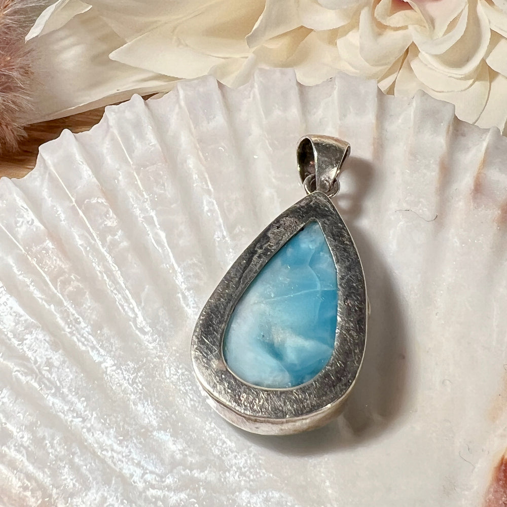 Hochwertiger Larimar-Anhänger in Tropfenform, gefasst in glänzendem Silber, präsentiert auf einer Muschelschale. Der himmelblaue Larimar-Edelstein mit natürlichen Farbverläufen und Maserungen verleiht dem Schmuckstück eine besondere Eleganz. Idealer Edelsteinanhänger für Damen, der maritimes Flair und eine spirituelle Note vereint – perfekt als stilvolles Accessoire oder besonderes Geschenk.