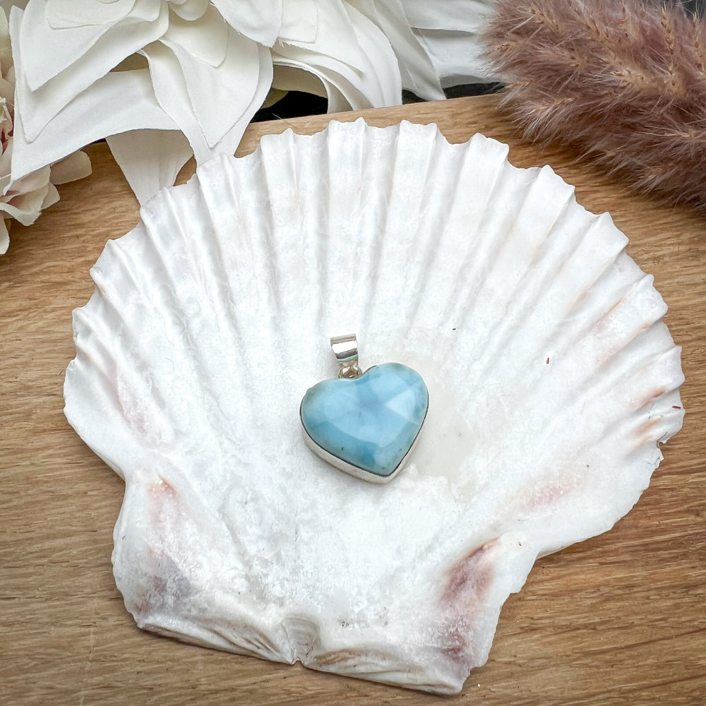 Herzförmiger Larimar-Kettenanhänger in 925er Sterlingsilber auf Muschelschale. Der blau-weiße Edelstein zeigt natürliche Muster und erinnert an das karibische Meer. Elegantes Unikat und perfektes Geschenk für Damen.